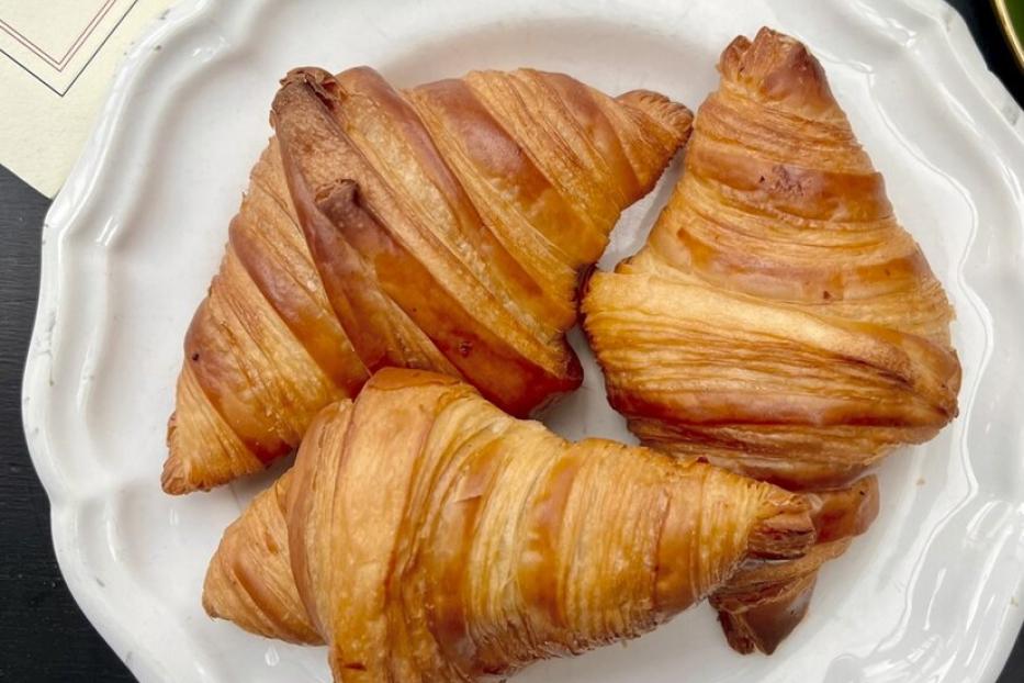Drei goldbraune, knusprige Croissants liegen auf einem weißen, gewellten Teller vor einem dunklen Hintergrund.