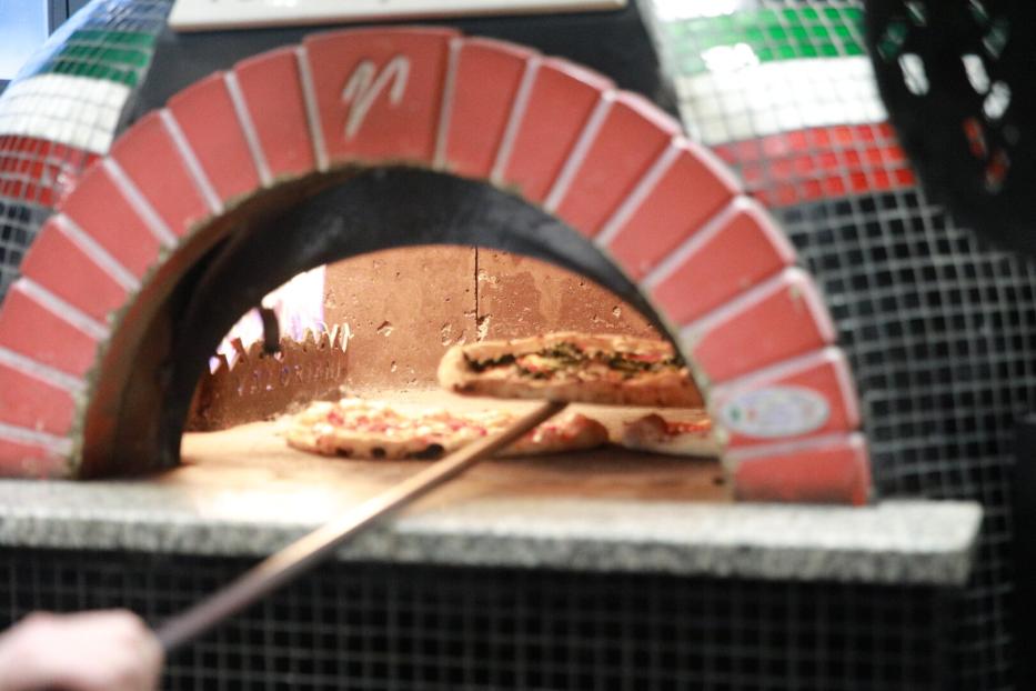Zwei Pizzen werden mit einer Schaufel in einem traditionellen Steinofen gebacken.