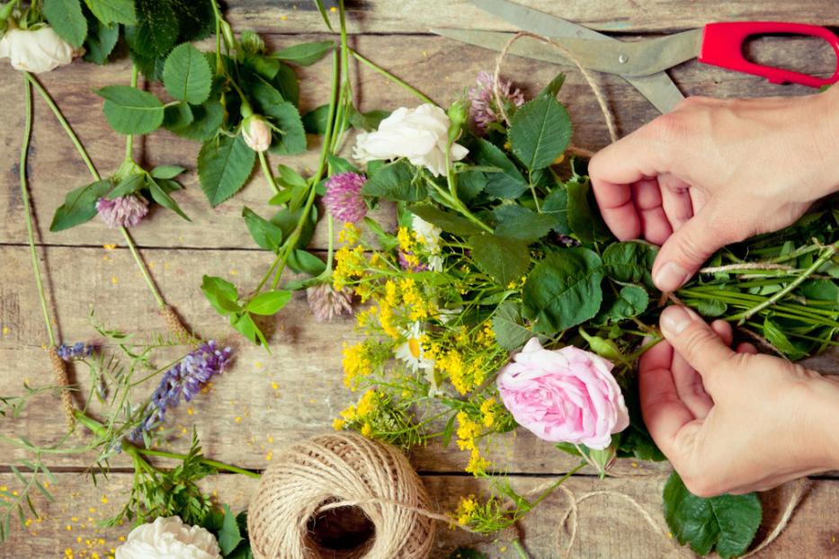 Eine Person bindet einen bunten Blumenstrauß auf einem Holztisch zusammen.
