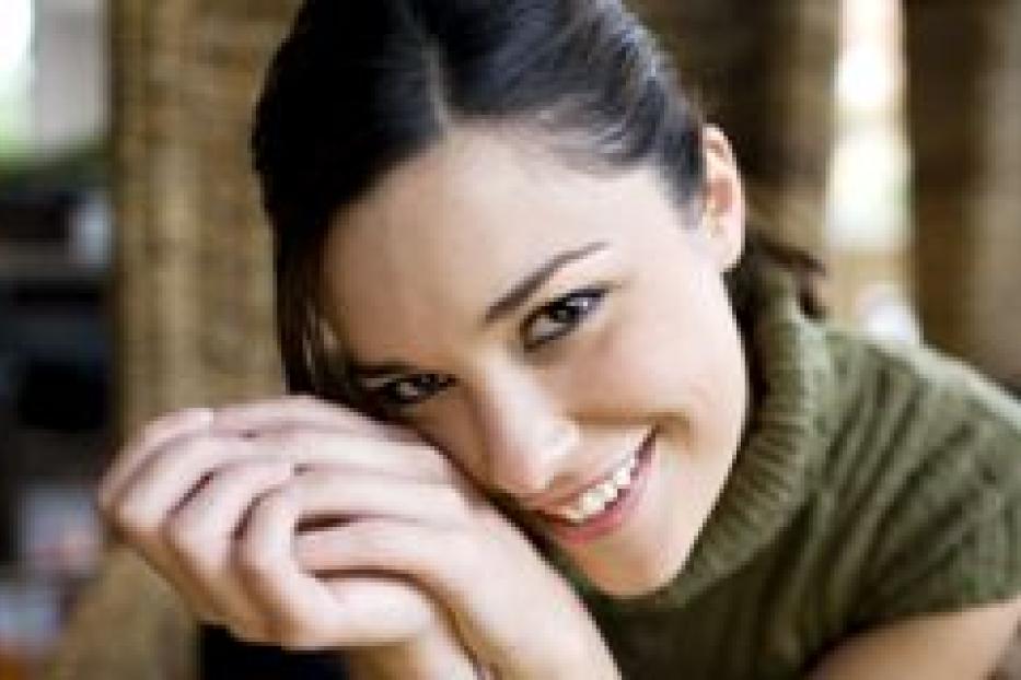 Eine lächelnde Frau mit dunklen Haaren und einem grünen Pullover blickt in die Kamera.