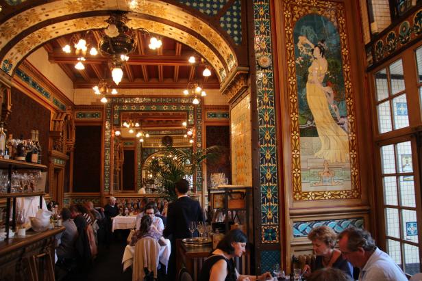 Ein belebtes Restaurant mit aufwendiger Jugendstilarchitektur und Gästen an den Tischen.