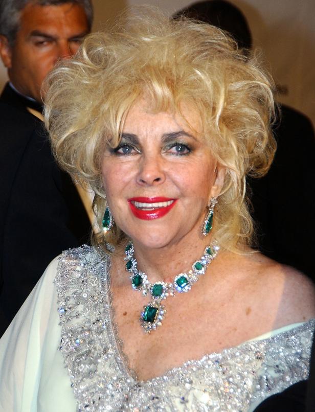 Elizabeth Taylor mit blonden Locken, smaragdgrüner Halskette und passenden Ohrringen lächelt.