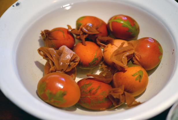 Orangefarbene Ostereier mit Pflanzenabdrücken liegen in einer Schüssel mit Wasser.