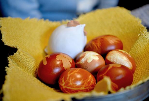 Rot gefärbte Ostereier liegen in einem Korb neben einer Keramikfigur in Hühnchenform.