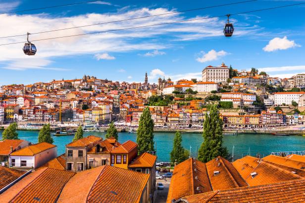 Stadtbild aus Porto, bunte Häuser am Fluss Douro, darüber eine Seilbahn mit Gondeln