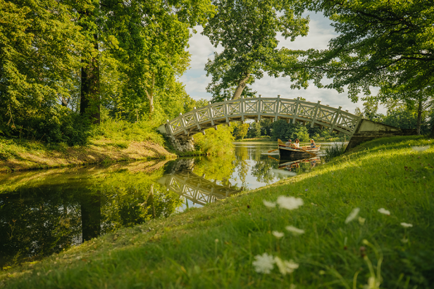 Park mit Bach und Brücke, Menschen rudern auf einem Boot unter der Brücke durch