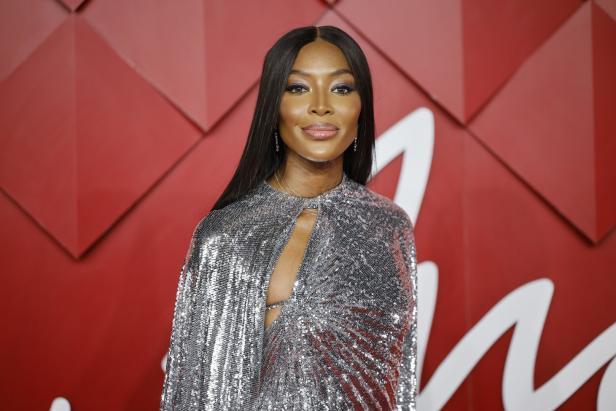 Naomi Campbell in einem glitzernden Cape vor einem roten Hintergrund.