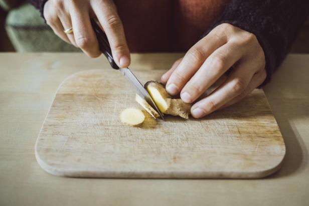 Woman's hands cutting ginger on wooden board, close-up - Stock-Fotografie