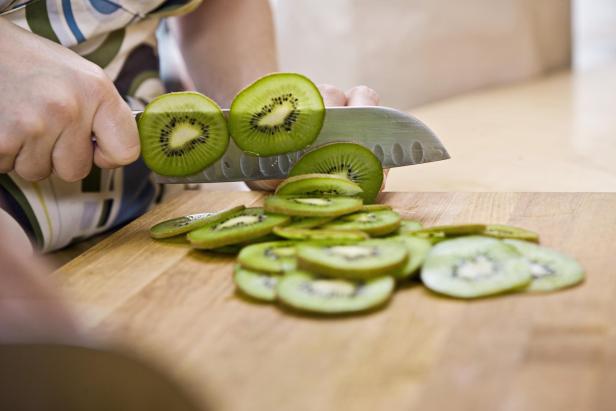 Hand slicing kiwi - Stock-Fotografie