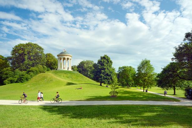 Eine Gruppe von Menschen, die auf einem grasbewachsenen Hügel mit Pavillon spazieren geht