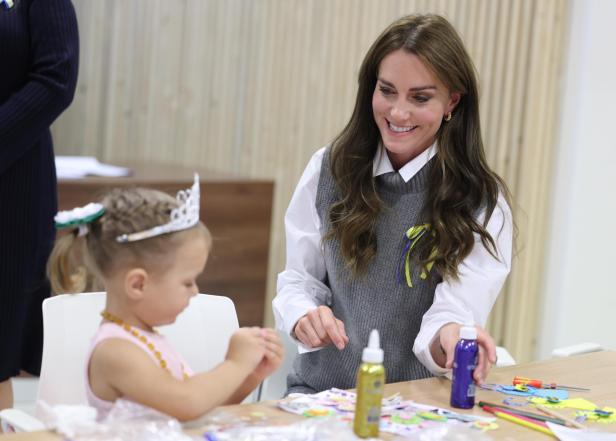 Prinzessin Kate im grauen Pollunder, bastelt mit einem kleinen Mädchen, das eine Prinzessinen Krone trägt 