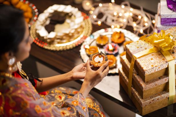 Frau in Indien, in traditionellem Gewand, hält eine Öllampe zu Diwali in der Hand, auf dem Tisch Öllampen und Geschenke zu Diwali