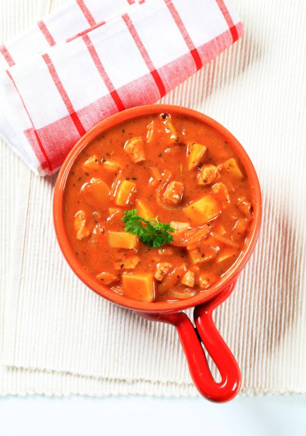 Veganes Erdäpfelgulasch in roter Casserole, veganes Essen, rotes Geschirrtuch