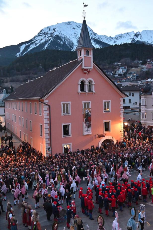 Viele Menschen beim Finale des Imster Schemenlaufens vor dem Rathaus kurz vor Sonnenuntergang. Publikum und Maskierte, im Hintergrund Berge