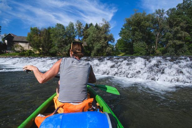 Frau in einem Kanu in Slowenien im Fluss Kolpa in der Region Bela Krajina bei Sonnenschein und blauem Himmel