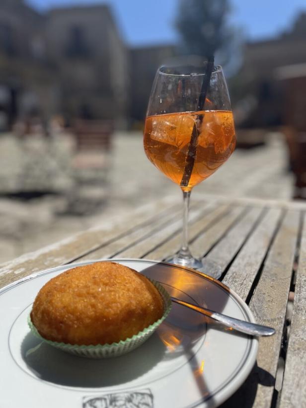  Arancina: Frittierten Reisbällchen aus Sizilien, gefüllt mit Fleischragout, Erbsen, Spinat, Mozzarella, daneben Aperol Spritz im Glas