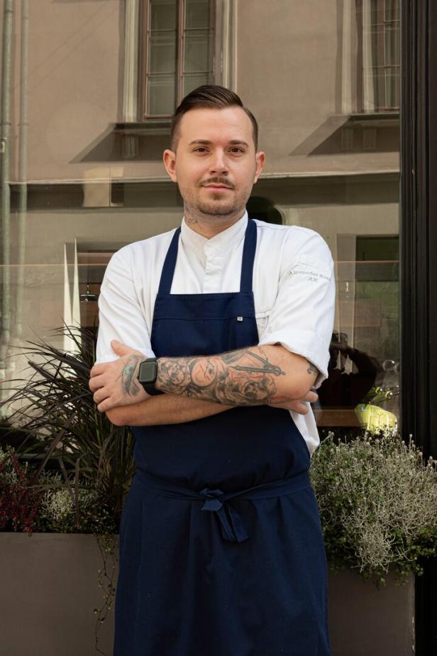 Der Küchenchef des Gasthaus - Artner auf der Wieden. Der Mann mit dem tätowierten Unterarm steht in Kochschürze vor seinem Lokal in Wien-Wieden v