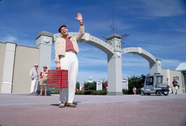 Jim Carrey als Truman aus dem Film Truman Show. Sein Charakter steht mit Koffer winkend auf rotem Pflaster und winkt, weil er verreisen will