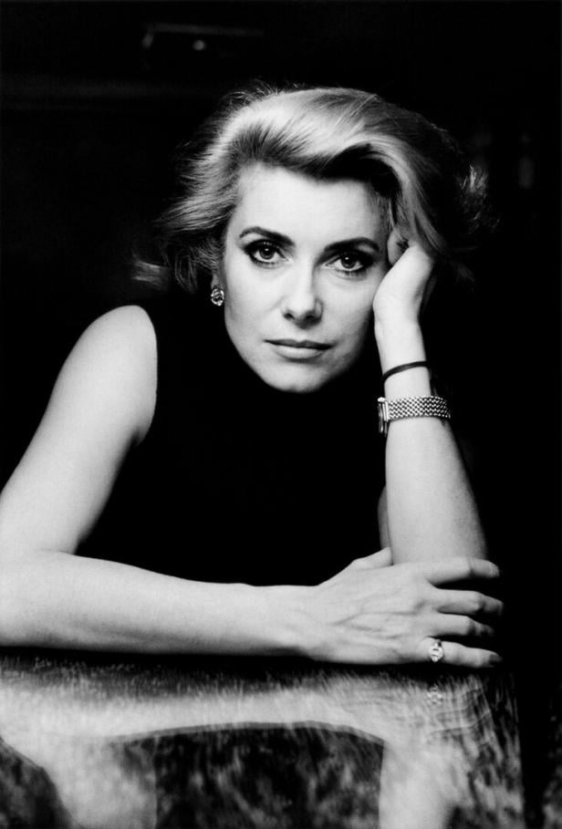 Eine Porträtaufnahme von Catherine Deneuve. Sie hat den Kopf auf ihre Hand gestützt und blickt etwas ernst drein