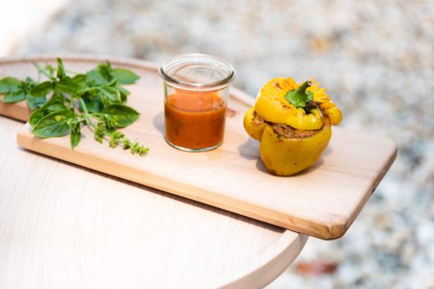 In einem kleinen runden Weck-Glas ist Gazpacho, daneben befindet sich eine gelbe, gefüllte Paprika und Kräuter auf einem Holzbrett