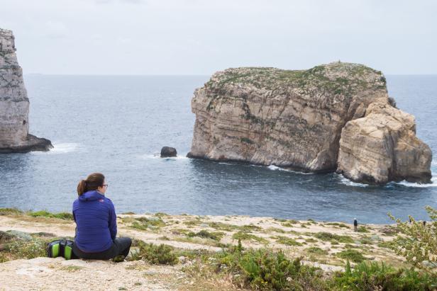 Frau sitzt an der Küste und blickt auf den Fungus Rock im Meer vor Gozo