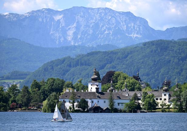 Ein Segelboot fährt vor dem Schloss Orth im Traunsee. Im Hintergrund bauen sich große Berge auf.