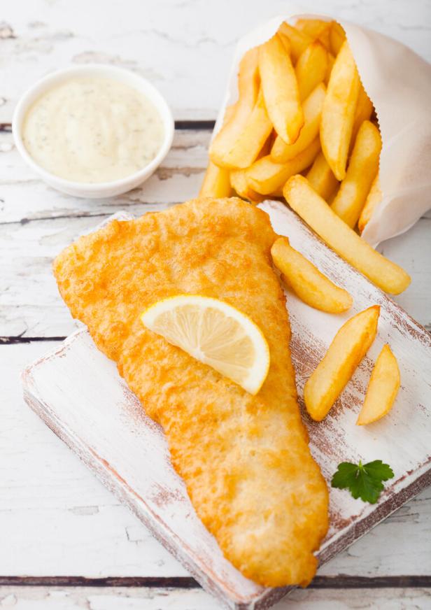 Traditional British Fish and Chips with tartar sauce on chopping board on white woode background.
