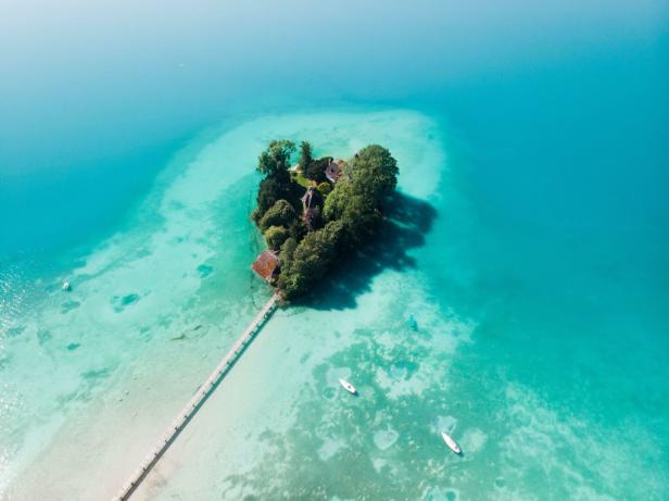 Luftaufnahme vom Attersee: ein Steg fürht zu einer kleinen, grünen Insel. Rundherum ist türkisblaues Wasser - Boote schwimmen darauf.