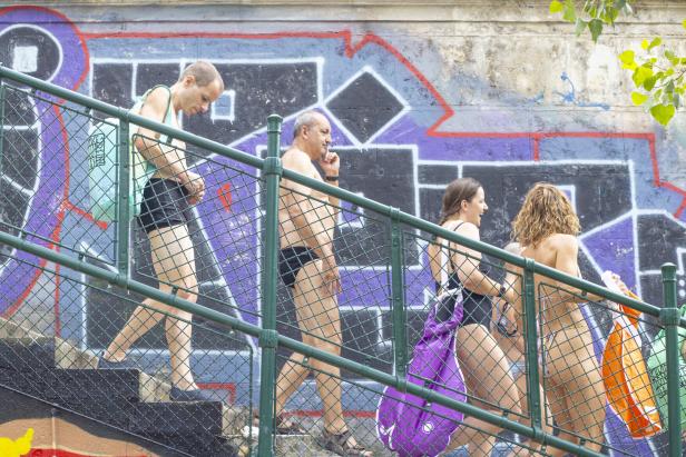 Menschen in Badebekleidung gehen eine Stiege hinab - entlang einer Mauer voll mit Graffiti-Schriftzügen