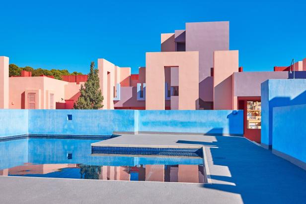 Eckige Gebäude in rosa und blauen Pastelltönen - davor ein gekachelter Pool