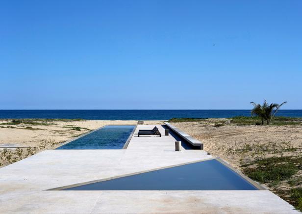 Eine betonierte Terrasse auf einem einsamen Strand. In sie sind zwei Becken eingelassen, ein rechteckiges und eines, das ein Dreieck bildet