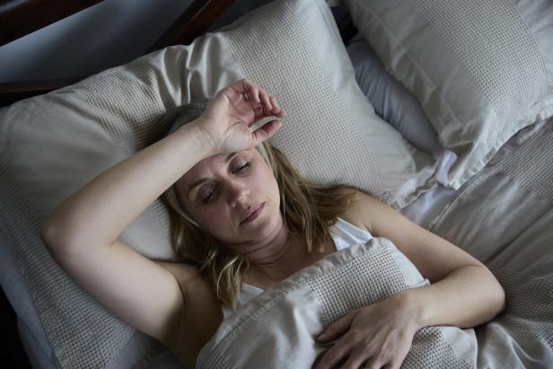 Eine Frau liegt im Bett und hält die Hand auf die Stirn.