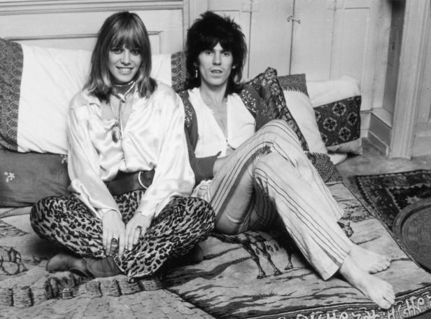 Anita Pallenberg und keith Richars sitzen auf Decken und Polstern am Boden. Sie hat eine Leopoardenhose und ein luftiges Hemd an, er einen lockere Leinenhose, ein Leinenhemd und eine Weste