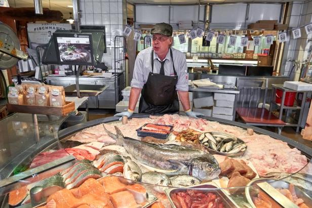 Ein Mann mit Schürze und Hut steht vor einer riesigen Platte mit verschiedensten Sorten Fisch.