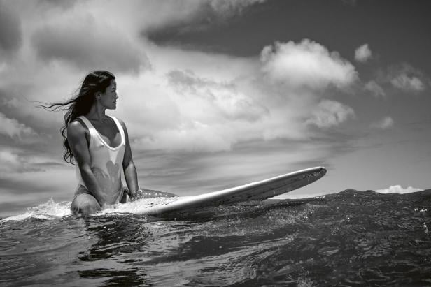 Eine Frau mit langen Haaren sitzt auf einem Surfbrett