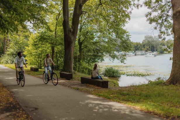 Zwei Fahrradfahrer fahren durch einen Wald mit einem See daneben. 