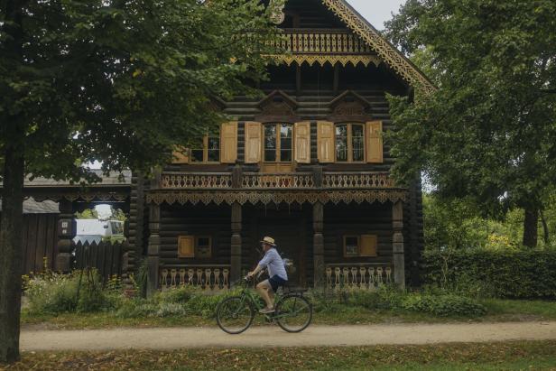 Ein Mann fährt mit dem Fahrrad an einem großen Holzhaus vorbei.