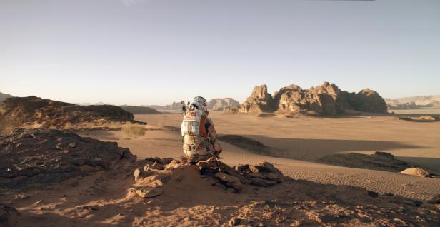 Szene aus dem Film Der Marsianer mit Matt Damon - Er ist als Astronaut von hinten zu sehen. Vor ihm liegt die Wüste des Mars.