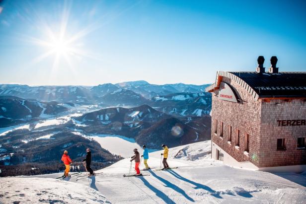 Skifahrer:innen auf einer Piste. Hinter ihnen die schneebedeckte Berglandschaft.