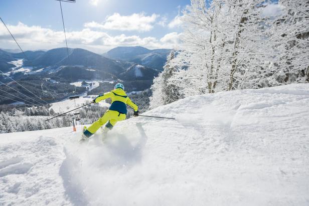 Ein Skifahrer in gelber Schneekleidung fährt bergab.