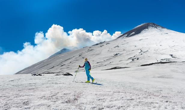 Mit Eine Frau geht bei schönem Wetter mit Tourenski auf den Krater des Ätna.