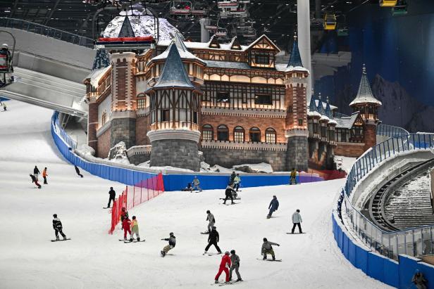 Wintersportler fahren auf einer Piste in einer Halle hinab. Mitten auf dem Hügel steht ein küstliches Schloss.