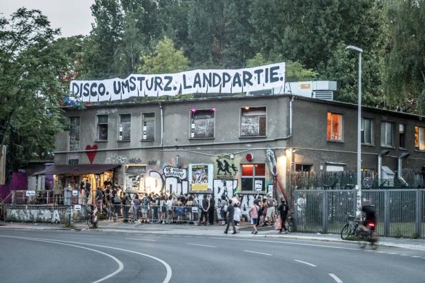 Menschen stehen am Morgen Schlange vor dem About Blank. Das Gebäude ist mir Graffiti und politischen Parolen besprüht. Auf dem Dach prangt ein Transparent mit der Aufschrift: Disco. Umsturz. Landpartie