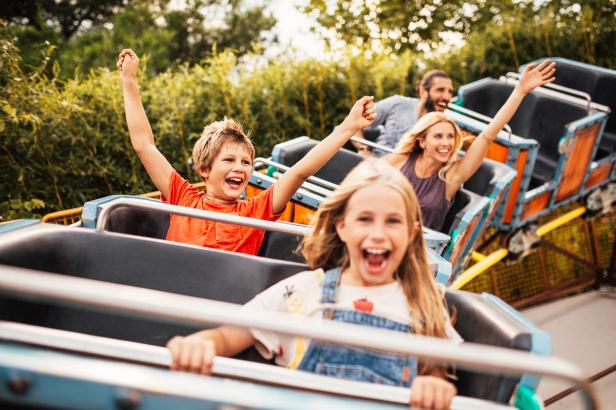 Kinder auf einer Achterbahn am Lächeln. Im Hintergrund ihre Eltern. 