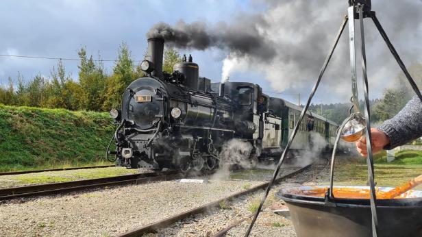Waldviertler Gulaschzug Ein Mann präsentiert einen Topf mit Speisen neben einem Gleis der Eisenbahn.