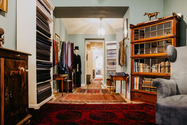 Maß-Salon Possanner Das Atelier mit Lehnstühlen, schweren Teppichen, Bücherregalen und einer Kleiderpuppe, die einen Zylinder aufhat.