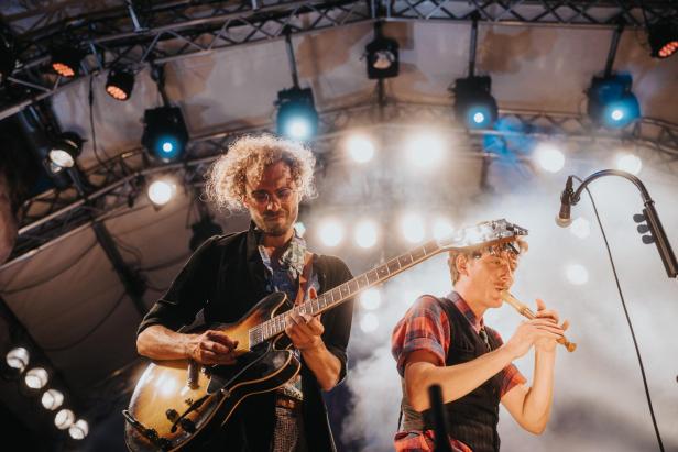Zwei Musiker stehen auf einer Bühne, einer singt und einer spielt Gitarre. 