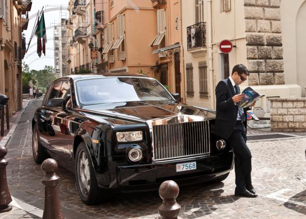 Chauffeur stands by Rolls Royce reading. Chauffeur stands by Rolls Royce reading.