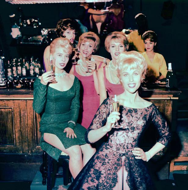 Eine Gurppe junger Frauen sitzt mit Champagnergläser in der Hand an der Bar
