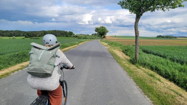 Eine Fahrradfahrerin zwischen grünen Wiesen und Feldern auf einer Landstraße